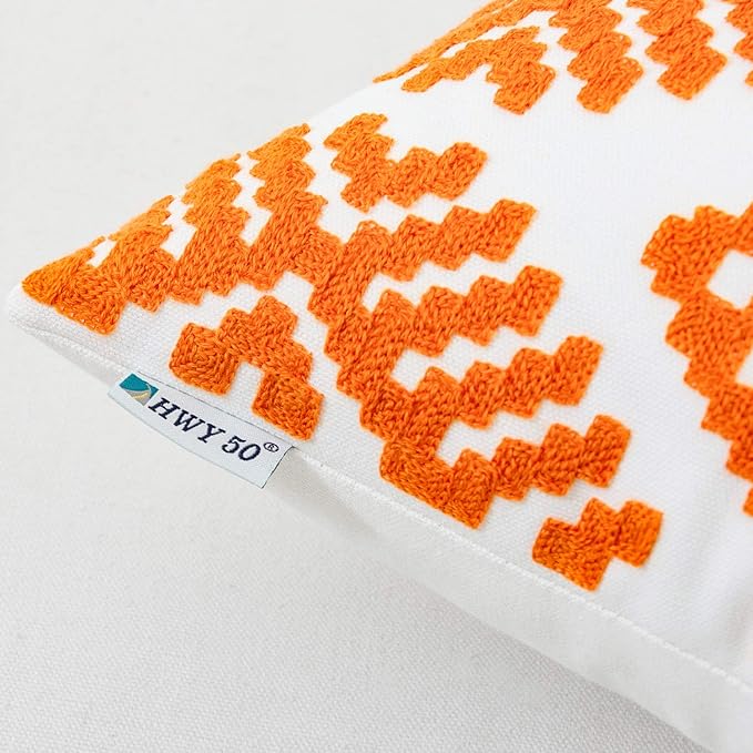 Orange embroidered throw pillow cover close-up with white geometric pattern and tag