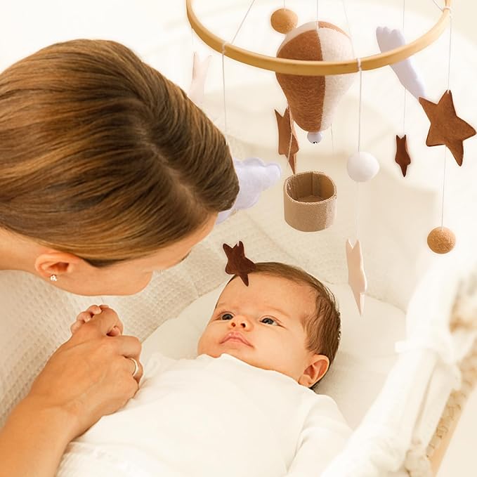 Baby and caregiver with a hanging hot air balloon and star mobile above the crib