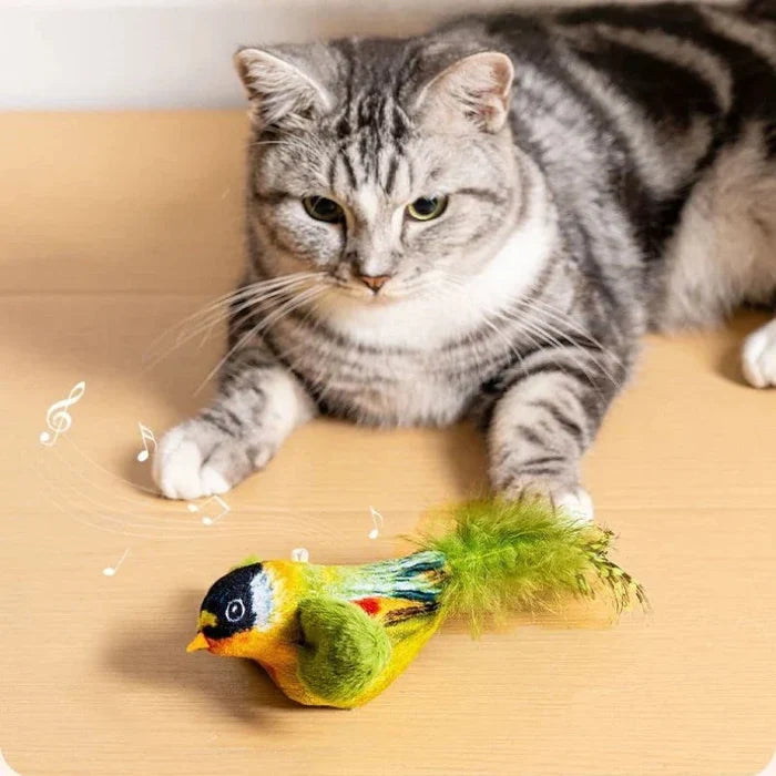 Gray cat playing with a green plush bird teaser toy on a wood floor