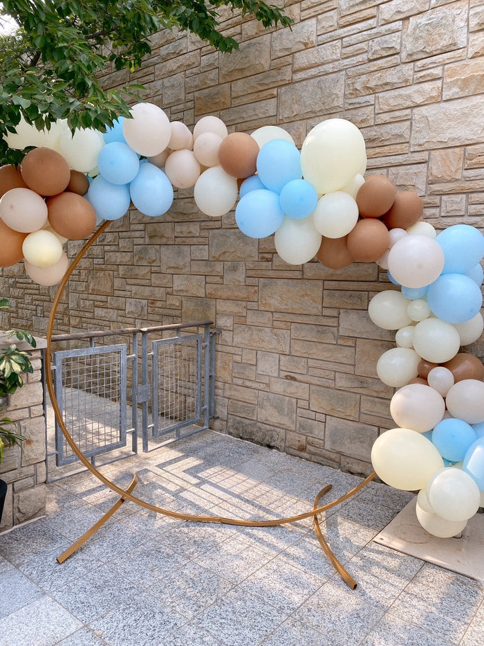 Multicolor balloon garland arch with cream, blue, and tan round balloons outdoors.