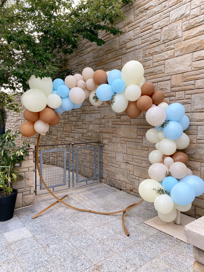 Pastel multicolor balloon garland arch with cream, blue, and brown round balloons.