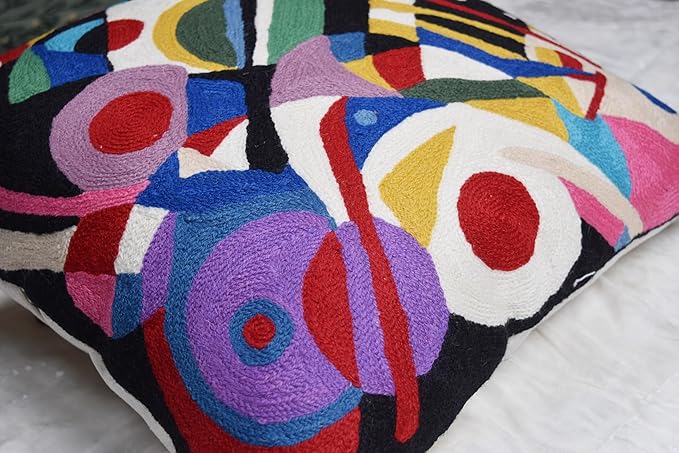 Black abstract embroidered pillow cover with colorful blocks and circular accents, angled view.