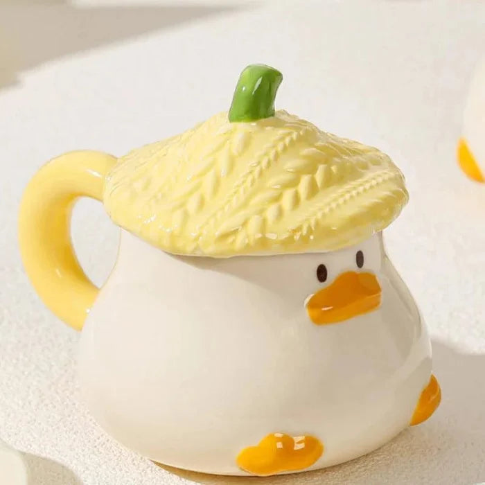 Duck-shaped ceramic mug with green-lidded yellow body, orange beak, and webbed feet