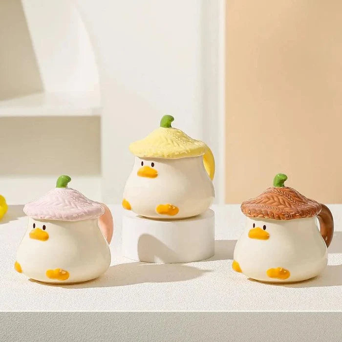 Duck-shaped ceramic mugs with lids in pink, green, and brown colorways, each with orange beak