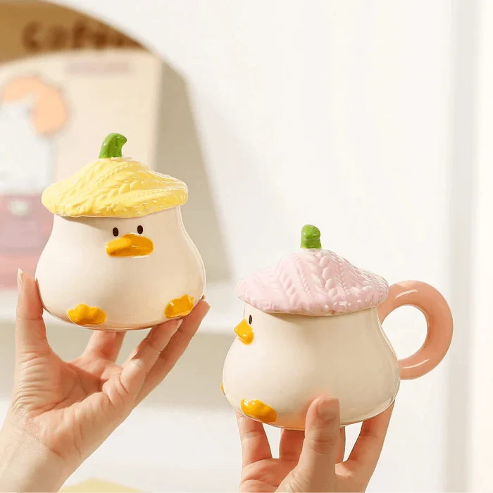 Duck-shaped ceramic mugs with pink and yellow textured lids, held in hands