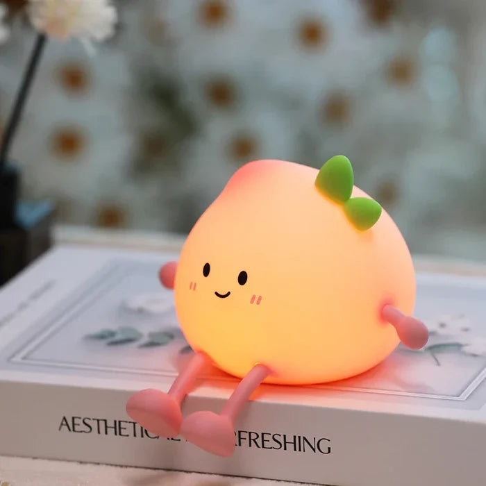 Peach-shaped night light with smiling face and green sprout, glowing on a book