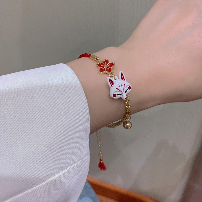 Red cord bracelet with gold chain, fox head charm and red tassel on wrist