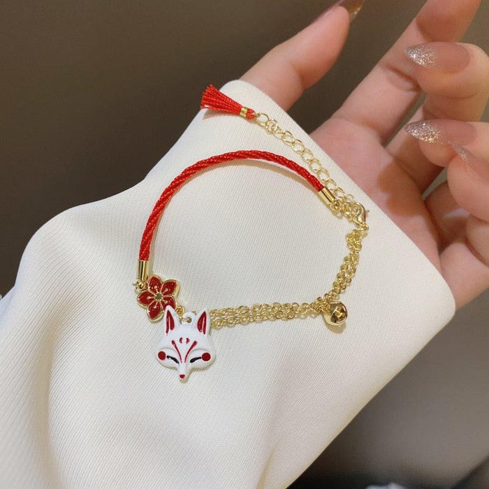 Gold chain and red cord bracelet with fox charm, red flower details and bell clasp