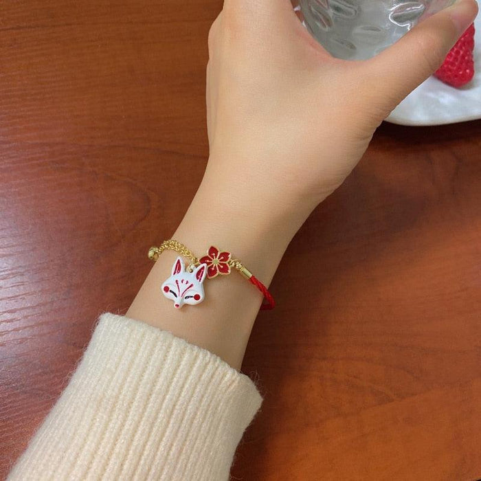 Fox bracelet with red cord and gold chain, red flower charm and fox head on wrist