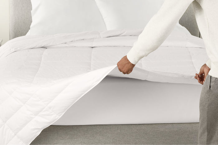 A person spreading the Down Duvet over a bed