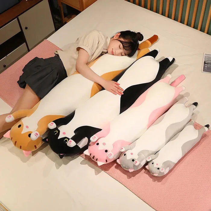 Long cat plush pillow, white body with black patches, orange tail and pink accents.