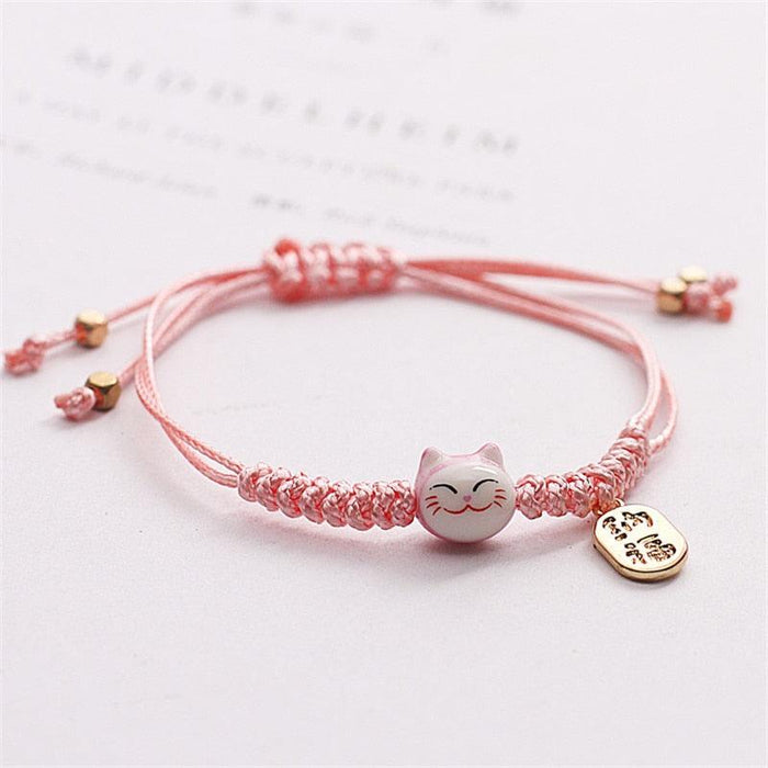 Pink braided bracelet with lucky cat charm and gold heart tag on adjustable string