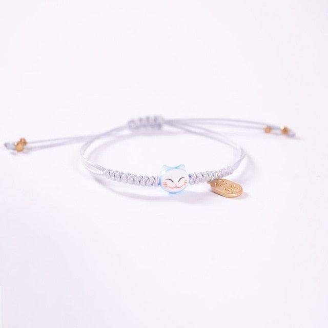 Light gray braided bracelet with blue cat charm and small gold coin tag