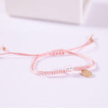 Light pink braided bracelet with cat face charm and small gold coin tag