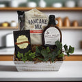 Breakfast gift basket with pancake mix, syrup bottle, chocolate mix packets, and decorative leaves
