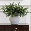 Artificial green Norfolk pine branch in a white speckled pot with dense needles