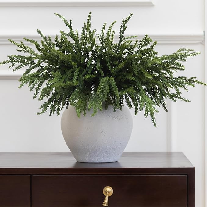Artificial green Norfolk pine branch in a white speckled pot with dense needles