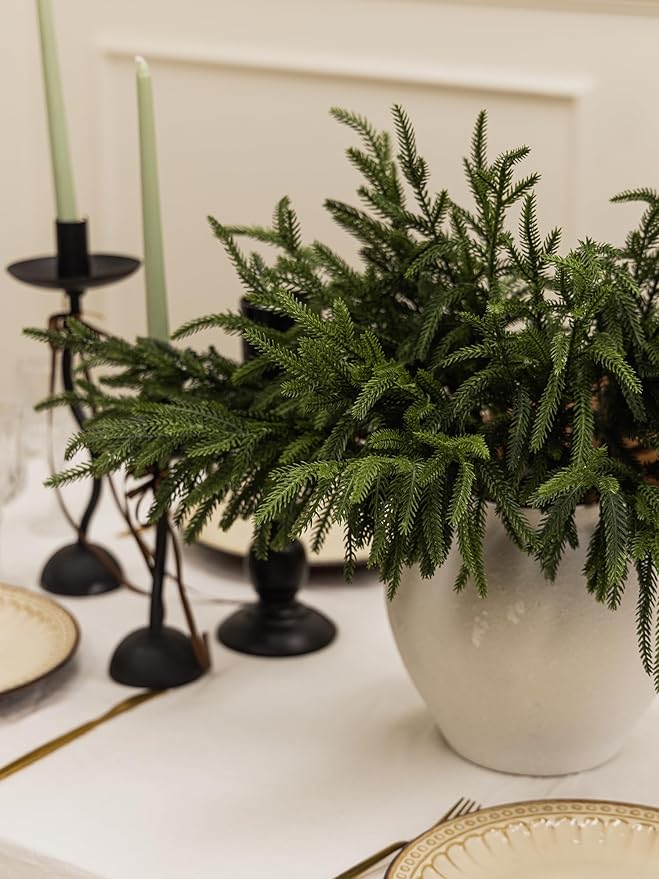 Artificial green Norfolk pine branch with layered needles in a white planter