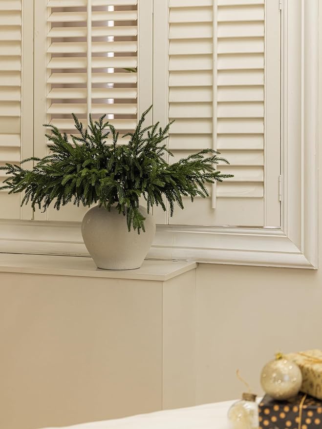Artificial green pine branch in a white pot displayed near window shutters
