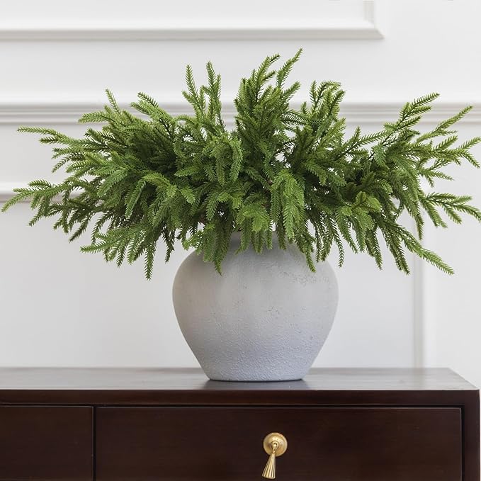 Artificial green Norfolk pine branch in a white speckled vase with full needle spray