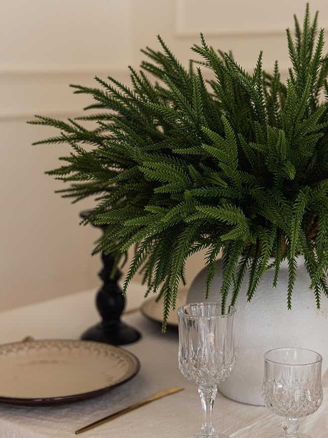 Artificial green pine branch centerpiece with dense needles in a clear glass vase