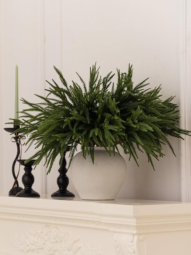 Artificial green Norfolk pine branch arrangement in a white planter on a shelf