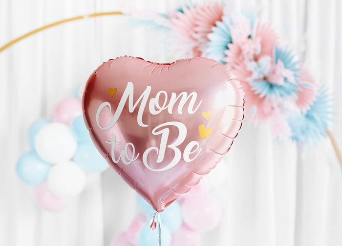 Rose pink heart balloon with “Mom to Be” text floating above party balloons.