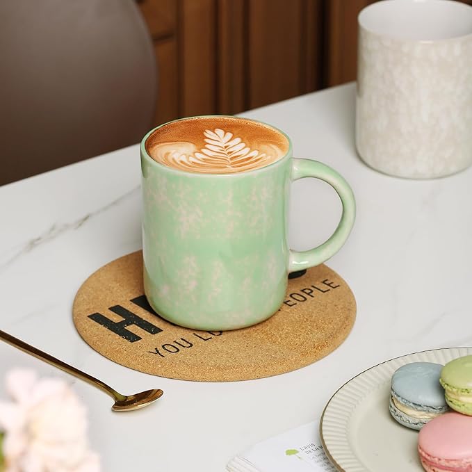 Speckled ceramic coffee mug with green glaze and curved handle, latte art on top