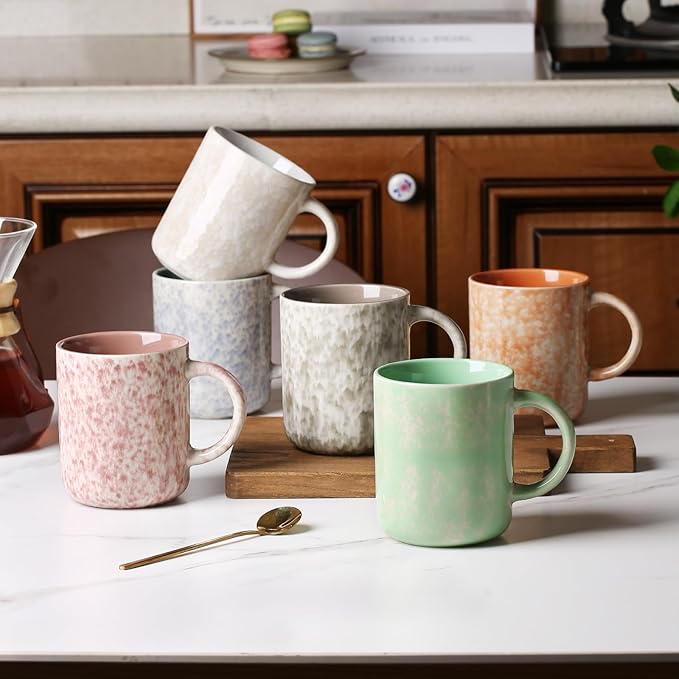 Set of 6 speckled ceramic mugs with curved handles, arranged on a countertop