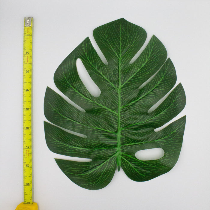 Monstera leaf cutout decoration, dark green with white slits; yellow measuring tape