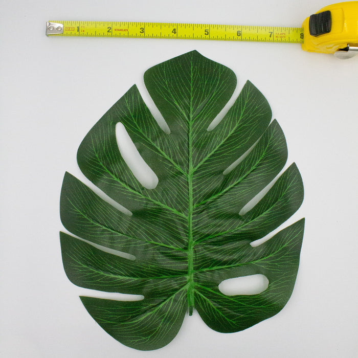 Monstera leaf cutout decoration, dark green with white slits; yellow tape measure