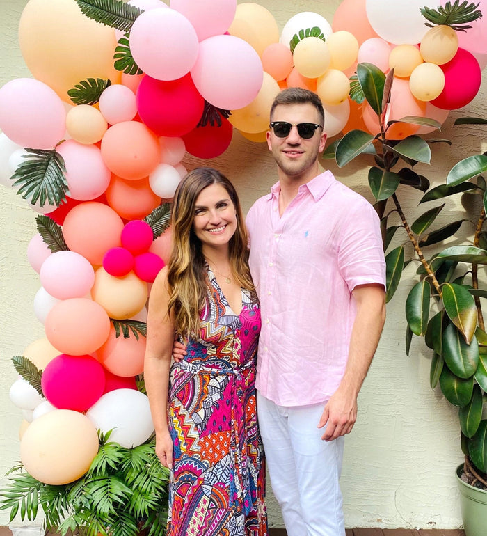 Monstera leaves and balloon party decor with people; green leaf accents by the backdrop