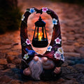Resin garden gnome couple holding a glowing solar lantern wreath with flowers