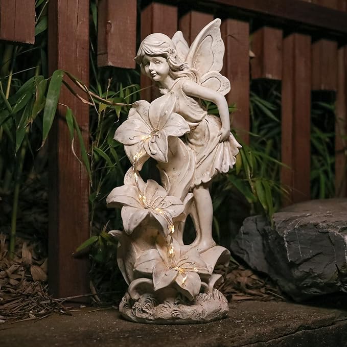 Tan resin outdoor fairy angel statue carrying large flower blooms, with warm LED lights