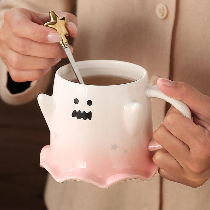 Ghost face mug with wavy mouth and gold star stirrer held near the handle; pastel pink base