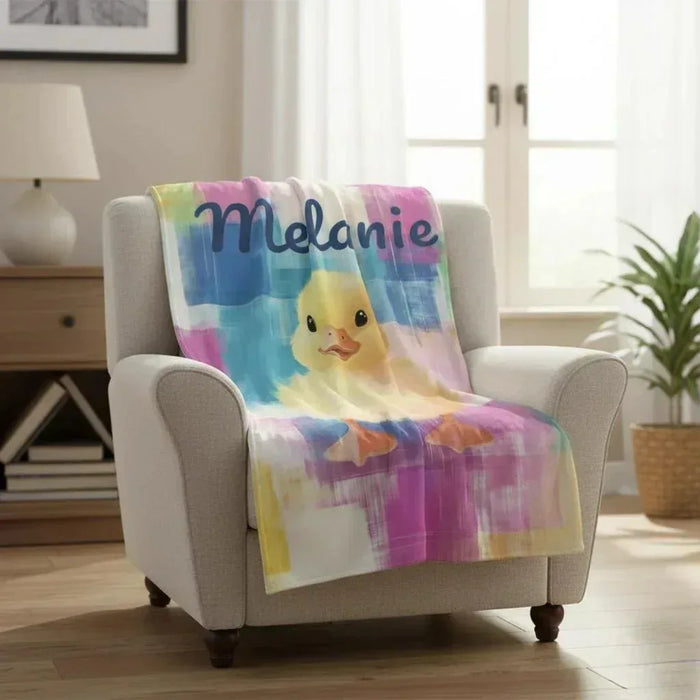 Personalized duckling blanket draped over light-gray armchair, colorful plaid and chick