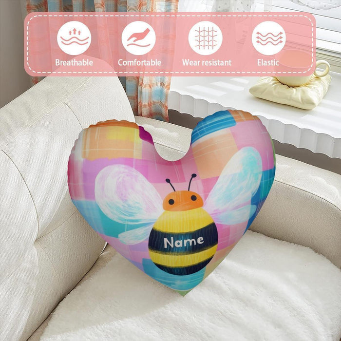 Heart-shaped plush pillow with bee design and custom name patch on couch cushion
