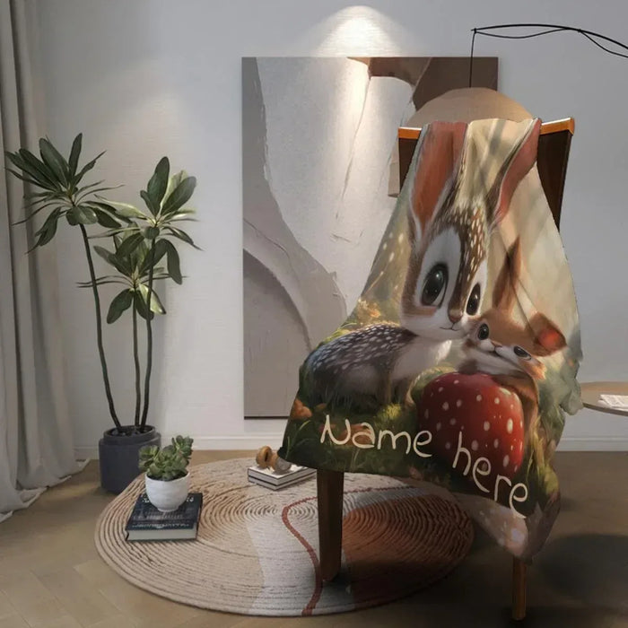 Personalized snuggle blanket on a chair with bunny and deer, red mushroom, “Name here”