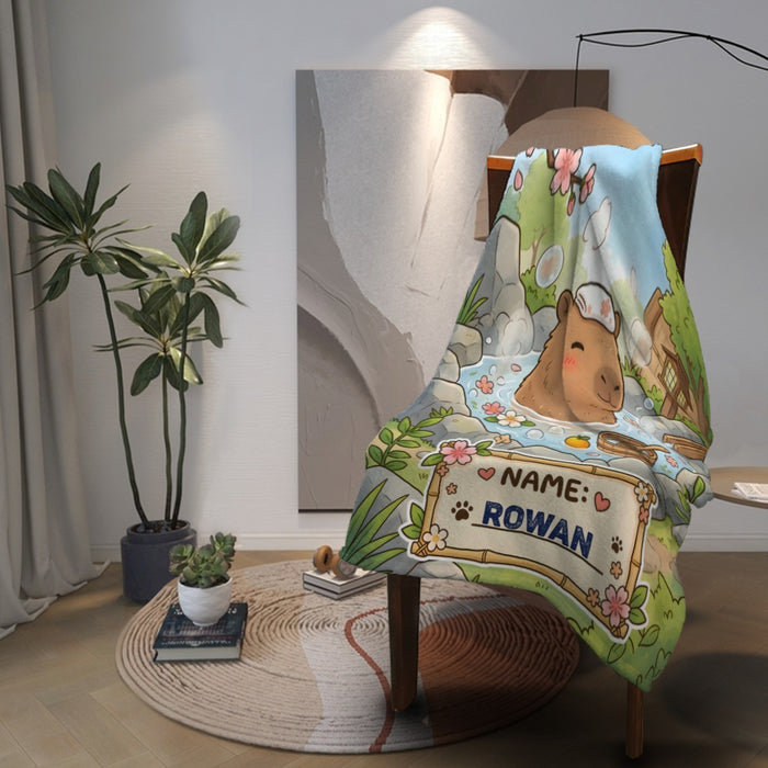 Personalized capybara hot spring blanket draped on chair with NAME ROWAN patch