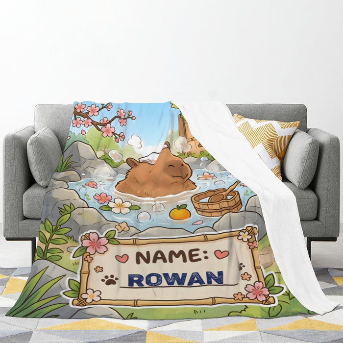 Personalized capybara hot spring blanket on sofa, custom name patch: NAME ROWAN