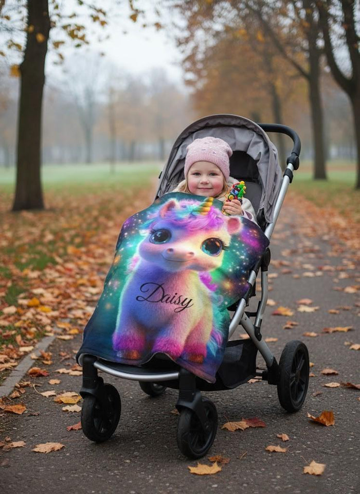 Rainbow unicorn blanket with name Daisy over a stroller seat on an autumn path
