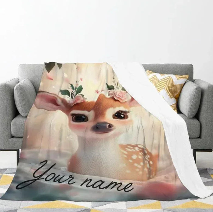 Deer face throw blanket with woodland plants and script text, folded on couch.