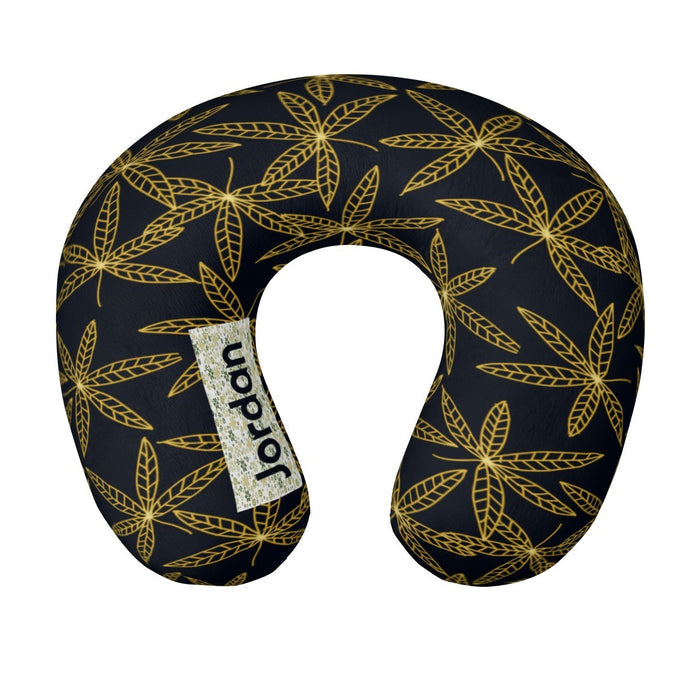Travel neck pillow in dark navy with gold botanical leaf pattern and side brand tag.