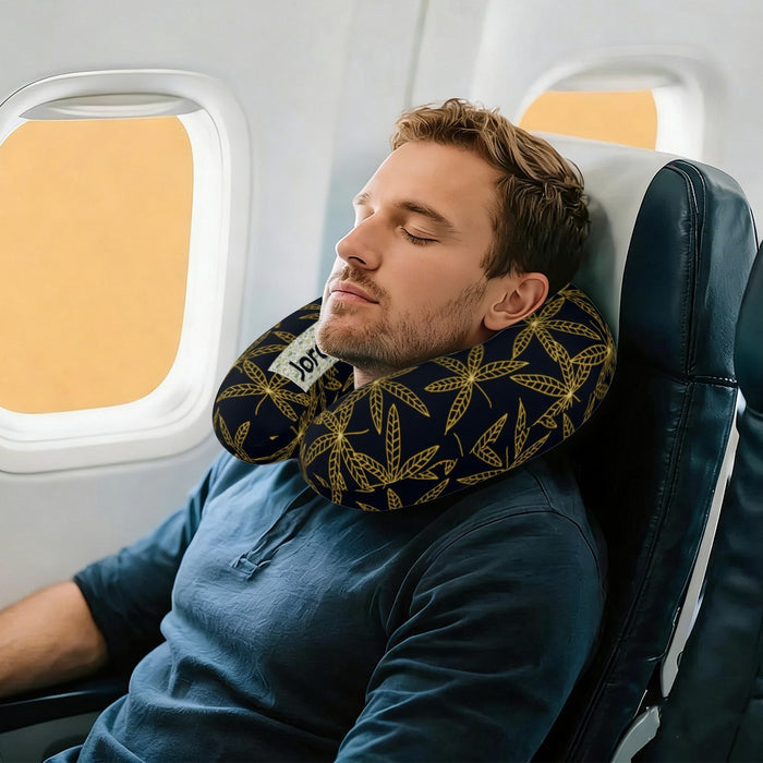 Travel neck pillow worn around a man’s neck, dark navy cover with gold botanical leaves.