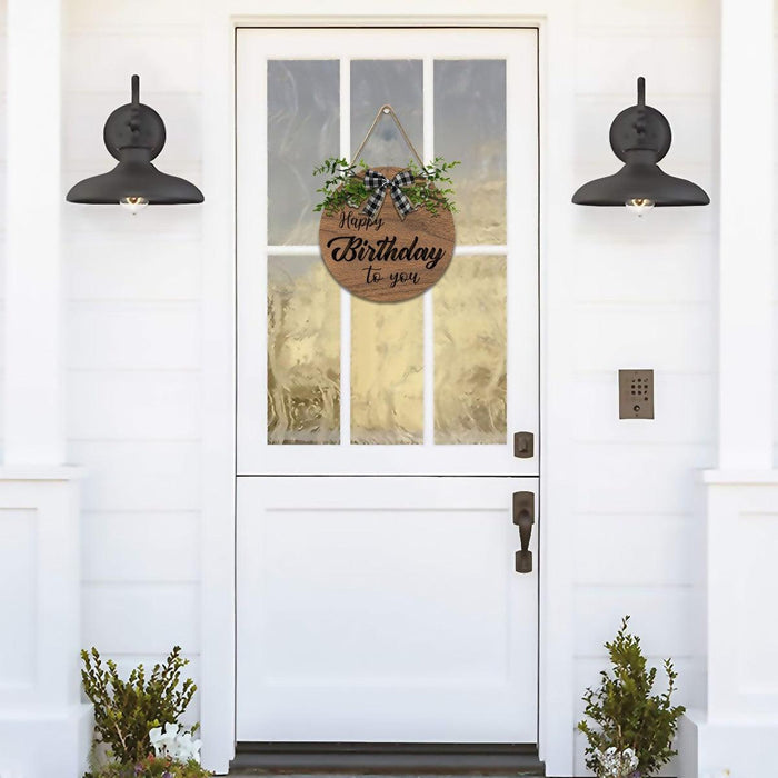 Wooden round Happy Birthday sign with greenery and black plaid bow hanging on door