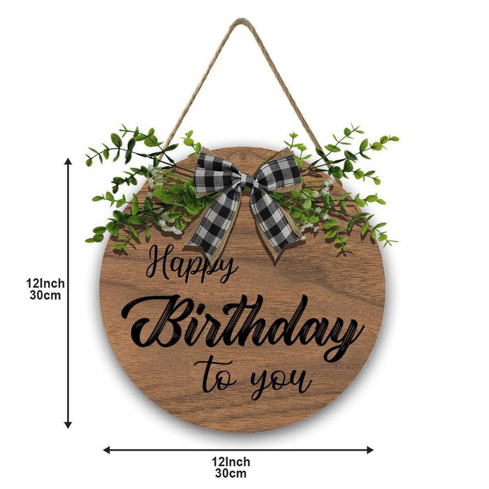 Wooden round Happy Birthday sign with linen bow, greenery sprigs, and rope hanger