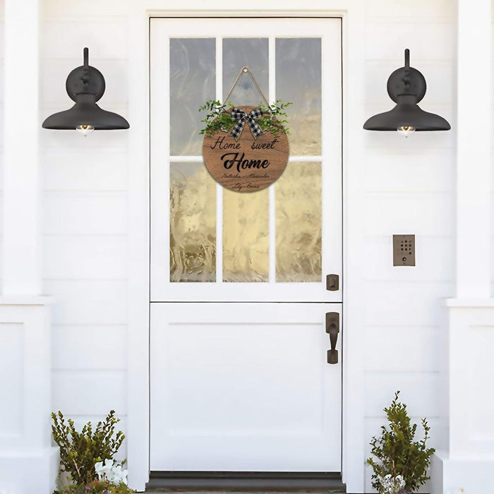 Round wooden hanging sign in doorway with “Home Sweet Home” script and plaid bow