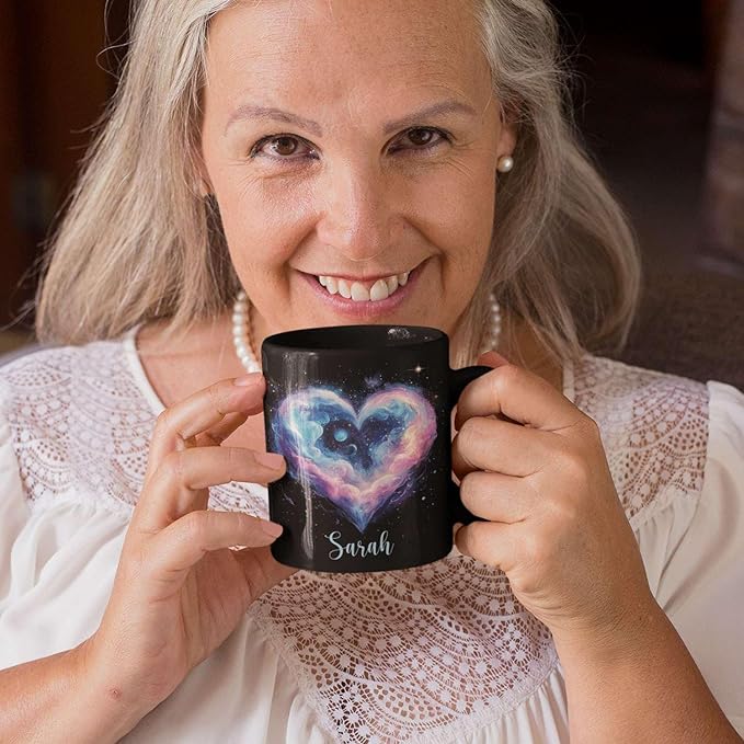 Smiling woman holding black ceramic mug with galaxy heart design and name Sarah