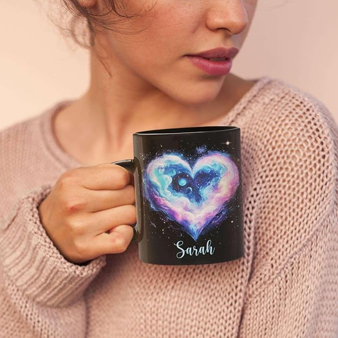 Woman sipping from black ceramic mug showing galaxy heart graphic and Sarah