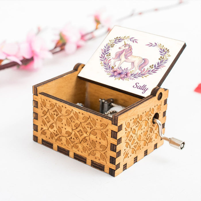 Wooden music box with hinged lid and unicorn illustration on top card, silver crank and ornate carving